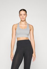Grå sportsbh med brede stropper og ribbet tekstur, parret med høyt midje svarte leggings. Enkelt design, tettsittende silhuett.