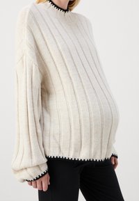 Ljusbeige, långärmad tröja med ribbad struktur, hög krage och svart kant vid hals och nederkant, designad för en lös passform.