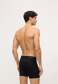 Czarne bawełniane bokserki o dopasowanym kroju z logo Calvin Klein na pasie, prezentowane na męskim modelu z tyłu.