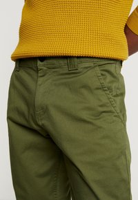 Gröna bomullstwillbyxor med smal passform, som har sidofickor och en mjuk textur. Tillsammans med en texturerad tröja i senapsgul stickad.