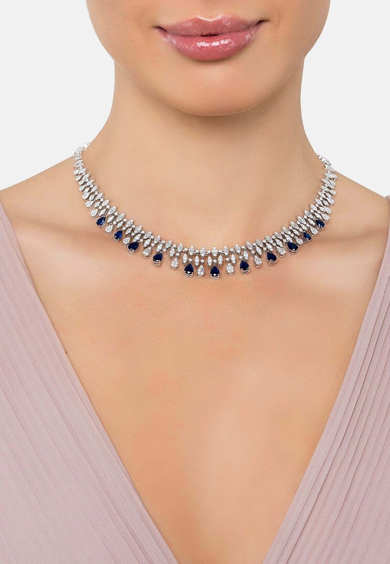 Silver-tone necklace featuring alternating clear and dark blue teardrop-shaped crystals, designed in a floral pattern, with a smooth texture.