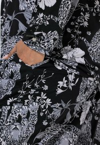 Sort stof med et blomster- og leopardprintdesign i grå og hvid, med en knappet manchet og en sidelomme.