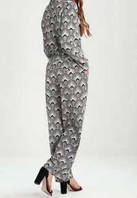 Kuvioitu mustavalkoinen haalaripuku, jossa on fanimuotoilu, pitkät hihat, rento istuvuus, sivutaskut, yhdistetty mustien korkokenkien kanssa.