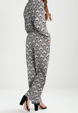 Zwart-witte jumpsuit met een fande sign, lange mouwen, relaxte pasvorm, zijzakken, gecombineerd met zwarte sleehakken.