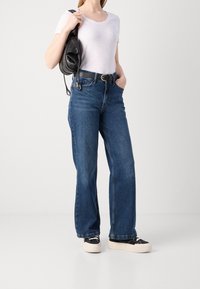 Denim jeans i lige snit, mellemblå vask, båret med en hvid bomulds t-shirt og en sort taske. Har sorte sneakers med en tyk sål.