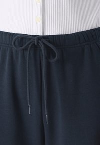Námornícke modré tepláky s šnúrkou na sťahovanie a štruktúrovaným pásom, skombinované s bielym rebrovaným topom s gombíkovými detailmi.