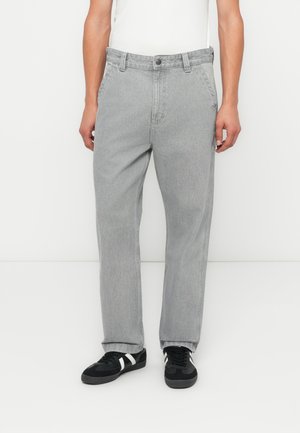 Jeans de mezclilla gris con corte recto, presentan un cierre de botón, diseño de cinco bolsillos y una textura suave. Llevados con zapatillas negras.