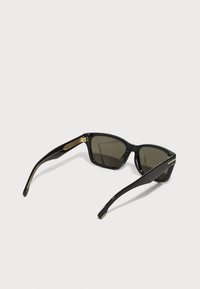 Gafas de sol negras con montura rectangular, lentes oscuros y acentos dorados en las bisagras. Acabado suave y brillante con brazos estrechos.