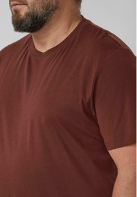 Brązowy t-shirt z krótkim rękawem, okrągłym dekoltem i lekko fakturowaną tkaniną. Na piersi subtelne logo.