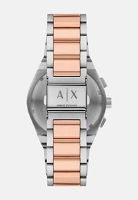 Hõbedane roostevabast terasest kell roosa kullaga aktsentidega rihmal. Omab ristkülikukujulist korpust ja klapi peal on löödud logo.