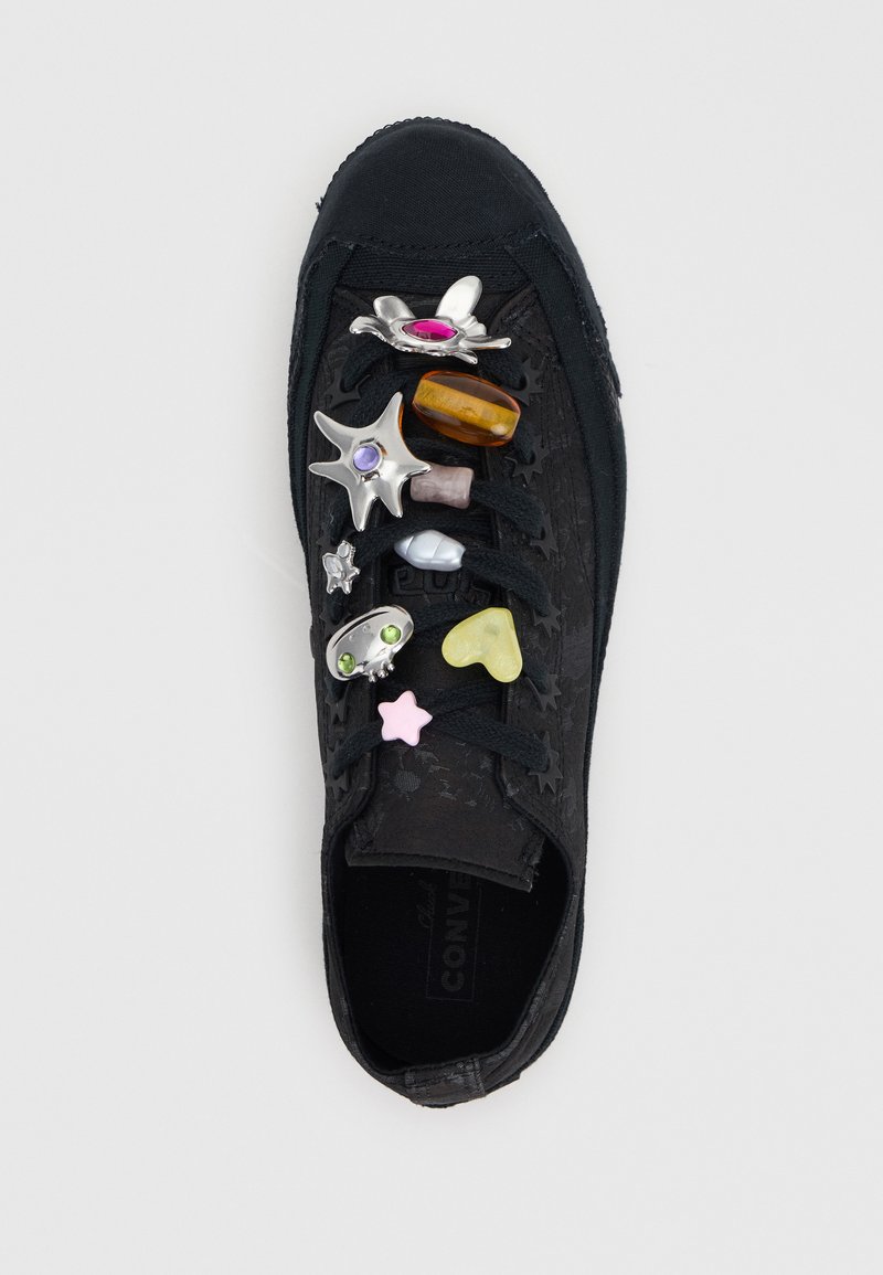 Black sneaker decorated with colorful star, heart, flower, and gem-shaped charms on the laces against a plain light background.