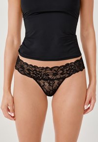 String noir en dentelle avec un motif floral et des bords festonnés. Matériau doux et transparent avec une bande unie assortie.