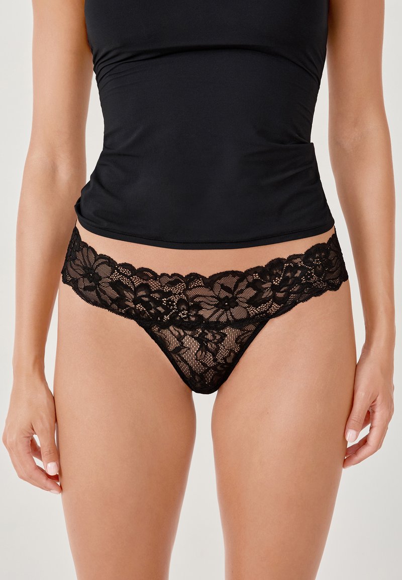 String noir en dentelle avec un motif floral et des bords festonnés. Matériau doux et transparent avec une bande unie assortie.