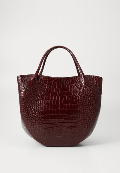 Τσάντα tote από δέρμα με εμβλήματα κροκοδείλου σε μπορντό απόχρωση, με στρογγυλή μορφή, διπλούς ιμάντες και χρυσό λογότυπο στη βάση. Λείος, γυαλιστερός υφή.