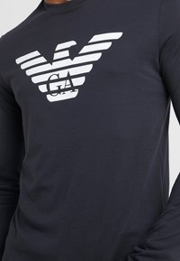 Marinblå långärmad skjorta i mjukt tyg med en vitrandig logotypdesign på bröstet, med en örnmotiff och initialerna "GA."