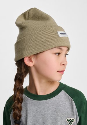 Olijfgroene gebreide beanie met een omslag, voorzien van een wit merkembleem. G gedragen met een grijs en groene raglan shirt, met gevlochten haar.