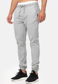 Pantalones jogger gris claro con puños elásticos, cinturilla con cordón y bolsillos laterales. Fabricados en un tejido suave con sutiles detalles de costura.