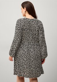 Schwarzes Kleid mit weißem Blumenmuster, langen Ärmeln, gerafftem Rücken und lockerer Passform. Leichtes Gewebe mit weichem Fall.