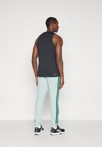 Μαύρο αμάνικο μπλουζάκι συνδυασμένο με ανοιχτό μέντα αθλητικά παντελόνια που διαθέτουν σκούρες πράσινες ρίγες στα πλάγια. Μαύρα αθλητικά παπούτσια ολοκληρώνουν την εμφάνιση.