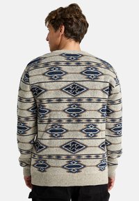 Suéter de punto con una superficie texturizada en color beige, adornado con patrones geométricos en azul y marrón, cuello redondo y puños y dobladillo acanalados.