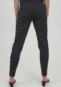 Svarta skräddarsydda byxor med smal passform, slät yta och två bakfickor. Avslutade med en medelhög midja och ankellång klipp.