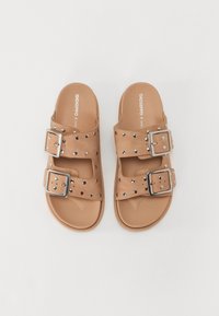 Chinelos tan com duas tiras largas, apresentando fivelas prateadas e detalhes com tachas. Feitos de material sintético com sola plana.