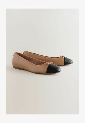 Beige ādas baleta kurpes ar melnu degunu, ar mazu loku priekšā un zemu, platu zoli. Gluda tekstūra kopumā.