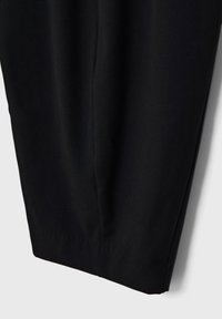 Pantalon noir avec une texture lisse, design à jambe fuselée et détails de plis subtils. Le tissu semble léger et doux.