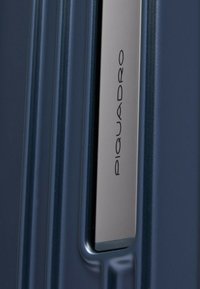 Blauer Hartschalenkoffer mit vertikalen Rillen, einem silbernen Metallgriff und einem geprägten Logo. Glatte Oberfläche aus strapazierfähigem Material.