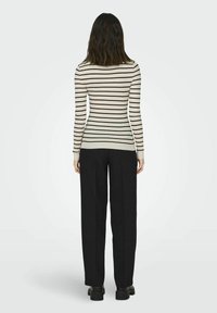 Haut à manches longues côtelé avec des rayures horizontales noires sur fond crème, associé à un pantalon noir à jambes larges et des chaussures noires épaisses.