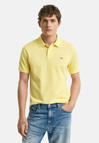 Gul polo skjorte lavet af bomuld, med en tre-knaps lukning, korte ærmer og et lille broderet logo på brystet. Båret med blå jeans.