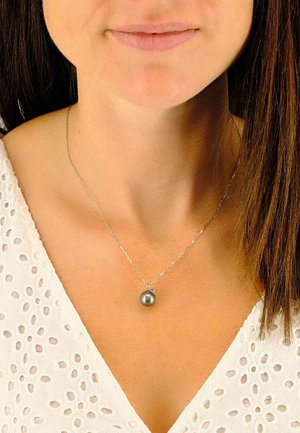 Collana con catena d'argento con un unico pendente a perla grigio scuro. La perla è rotonda con una texture liscia, indossata su un vestito chiaro.