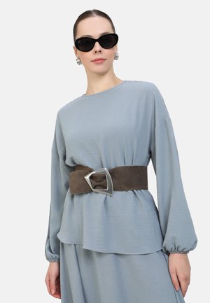 Light blue top with long sleeves, textured fabric, layered design, secured with a brown suede belt featuring a silver, angular buckle.