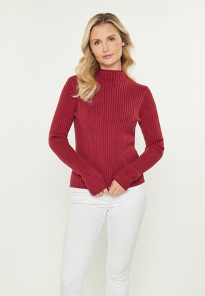 Rød ribbet turtleneck sweater med lange ærmer og tommelhulsmansjetter, parret med hvide jeans. Glat tekstur, tætsiddende design og ensfarvet.