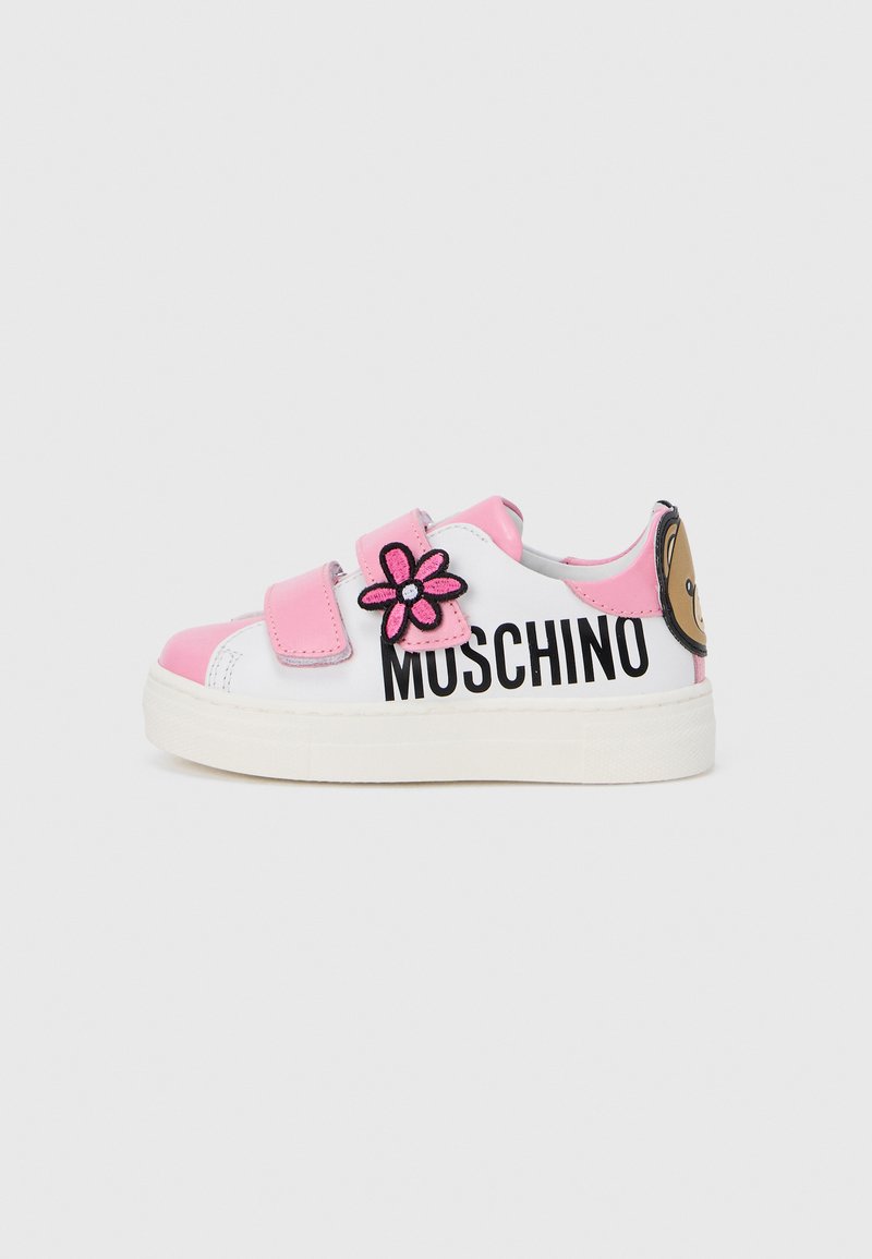 Baskets blanches avec accents roses, brides en velcro, lettrage noir "MUSCHINO", une application fleur rose et un motif d'ours sur le talon.