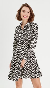 Abito camicia geometrico in bianco e nero con maniche lunghe, chiusura a bottoni, colletto e gonna svasata, realizzato in tessuto leggero.