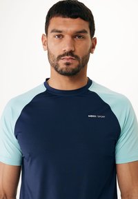 Námořnické modré sportovní tričko s světle modrými raglánovými rukávy. Má logo na hrudi, je vyrobeno z prodyšného materiálu s hladkou strukturou.