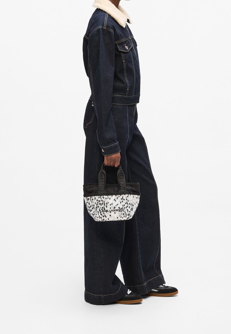 Personne vêtue d'une veste en jean foncé avec un col en shearling blanc et un jean à jambes larges, tenant un sac à main Karl Lagerfeld noir et blanc.