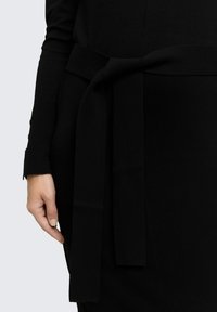 Schwarzes Strickkleid aus strukturiertem Material, mit langen Ärmeln und einem gebundenen Taillengürtel. Das Kleid hat eine taillierte Silhouette mit einer glatten Oberfläche.
