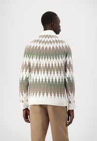 Strickpullover mit geometrischem Muster in Braun, Weiß und Grün. Hoher Kragen und gerippte Bündchen. Strukturierter Stoff verleiht Tiefe.