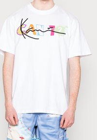 Camiseta de algodón blanca con texto multicolor y divertido "CAN?" junto a una línea negra dibujada a mano. Mangas cortas y corte relajado.