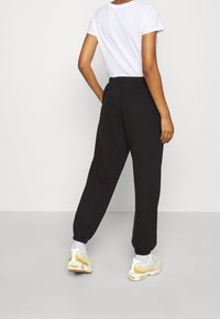 Svarta joggerbyxor med elastiskt midjeband och avsmalnande muddar, tillsammans med en vit t-shirt och ljusgula sneakers.