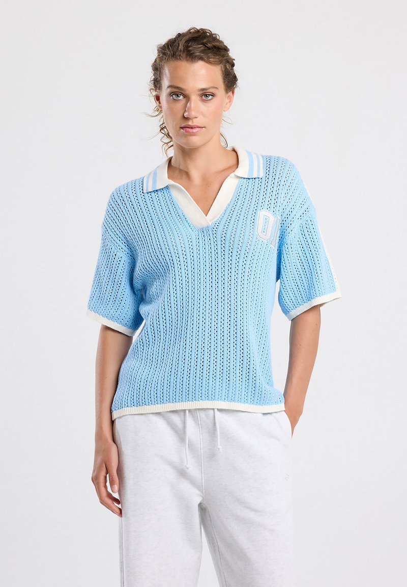 Light blue short-sleeved polo sweater with a V-neck, ribbed texture, white trim, and a small logo patch on the left side.