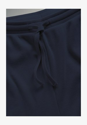 Közelkép tengerészkék bordázott szövetből készült nadrágról, amelynek derékrészén megkötött zsinór van.