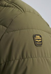 Olive green puffer jacket with a smooth texture, featuring a black and gold logo patch labeled "PME Legend American Classic."