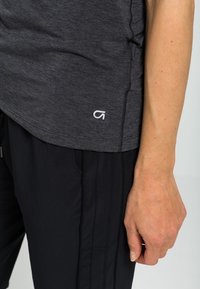 Haut de sport gris à texture lisse avec un logo sur l'ourlet, associé à un pantalon de sport noir avec des coutures verticales.