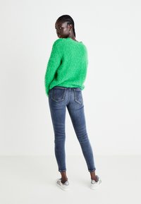 Vihreä pörröinen neule, jossa on väljä malli, yhdistettynä tummansinisiin kapeisiin farkkuihin, joissa on erottuvat takataskut ja vaaleat tikkaukset.