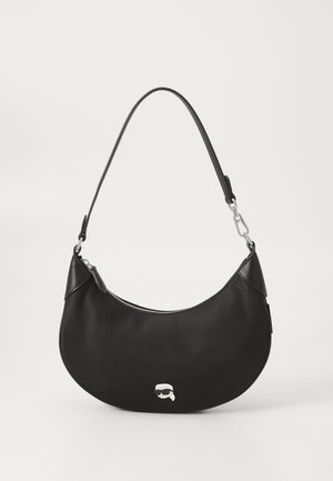 Sac à main noir structuré avec un design courbé, texture lisse, quincaillerie argentée et un détail de logo sur le devant. Bretelle ajustable incluse.