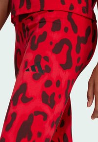 Leggings rojos con un estampado de leopardo negro, fabricados en un tejido elástico. Incluyen un acento del logo negro de Adidas en el costado.