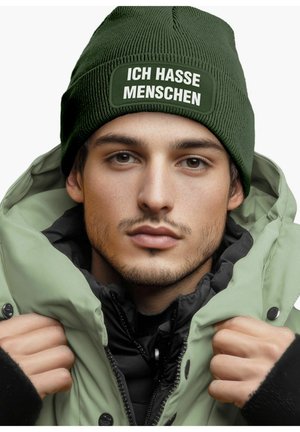 Green knitted beanie with white text reading "ICH HASSE MENSCHEN" paired with a light green puffer jacket and a black inner layer.